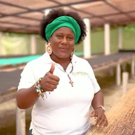 Person wearing a white shirt with a Corpoteva logo, giving a thumbs-up gesture in an outdoor setting.